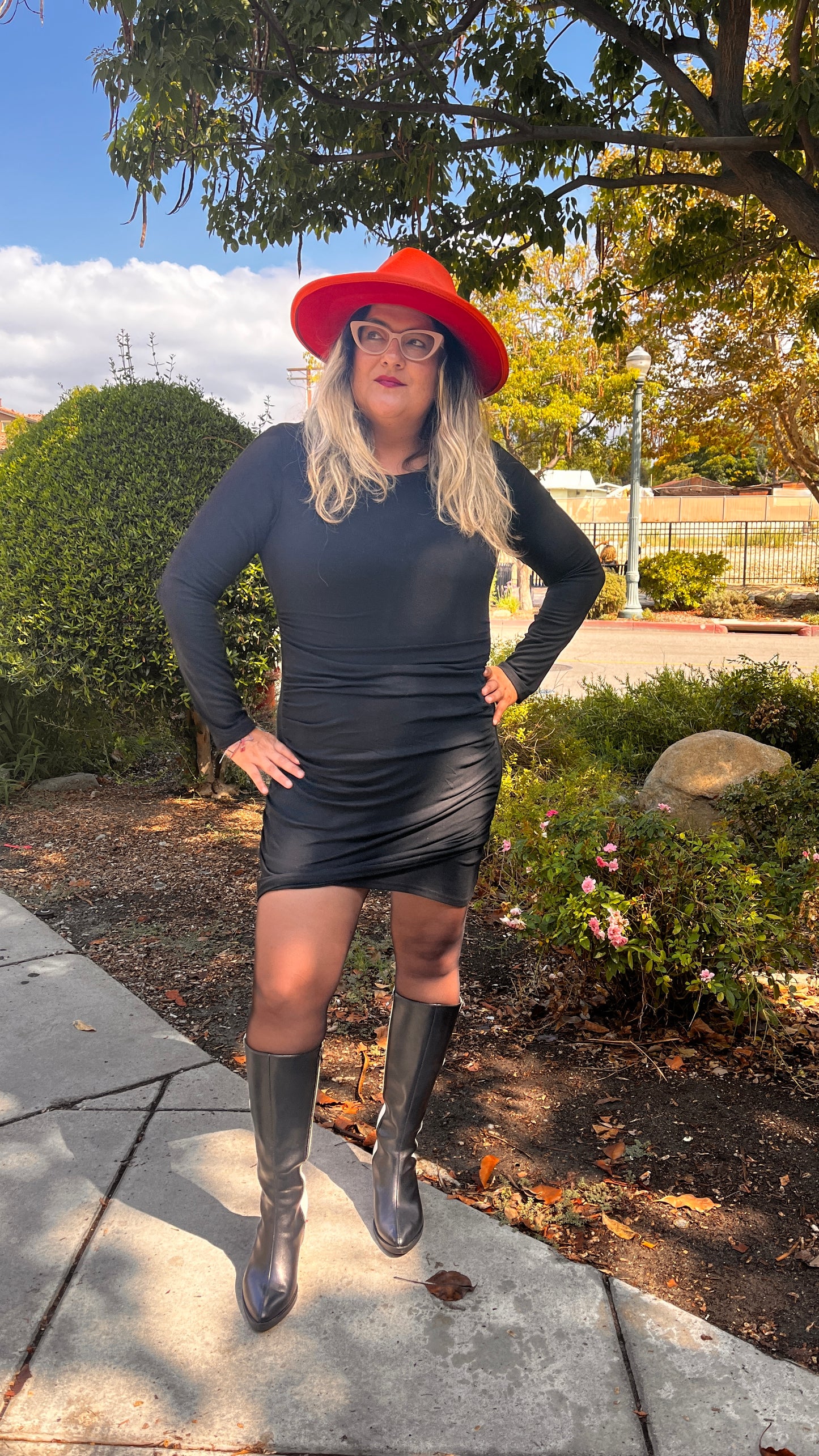 model in size large of a little black mini dress wearing bottom and red fedora hat outside claremont village