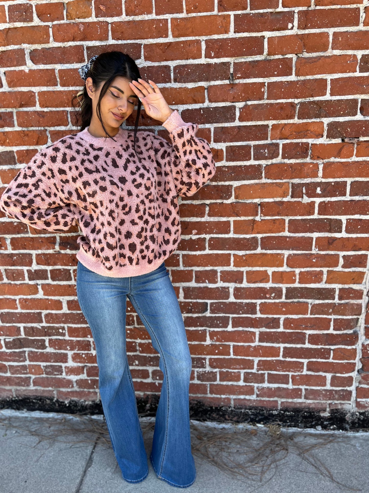 trendy girl wearing a leopard sweater with bell bottoms posed against a brick wall